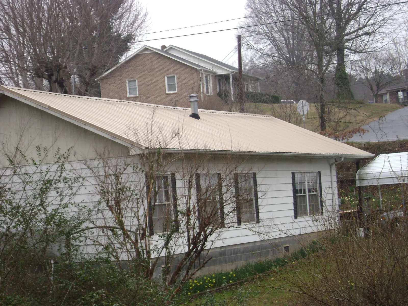 Tan metal roof on a white sided house set into a hillside — Commercial Roofing by Roofing Brothers in Garfield
